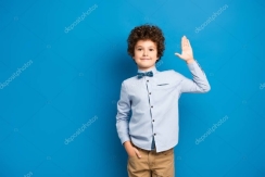 Радостный ребенок в рубашке и галстуке-бабочке стоит с рукой в кармане и  машет рукой на синий #417874290 - Ларасток